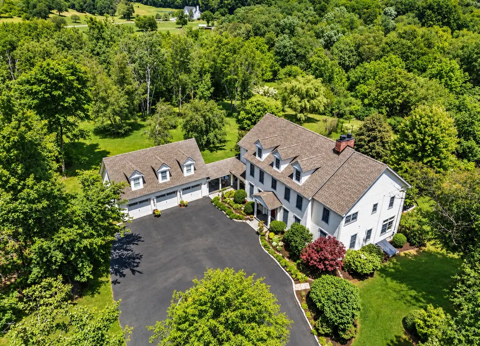 Aerial view of a white colonial with an attached garage on a Hudson Valley estate